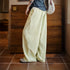 Person wearing light-colored wide-leg pants and a dark top in a room with wooden walls and tiled floor.